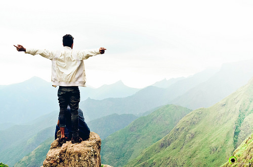 Man standing on cliff with arms raised high.